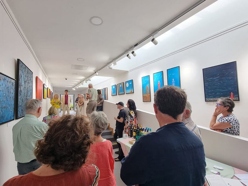 A large group of people listening to the guest-speaker and artist at the art gallery
