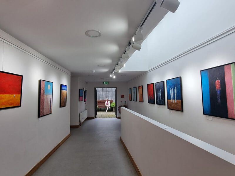a view inside the art gallery. In the distance we see the artist seated on a bench