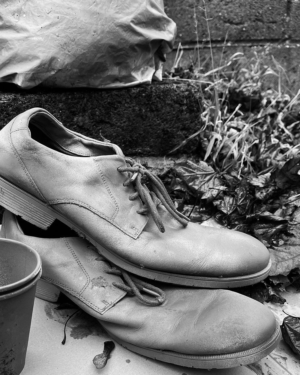 Close up of an old pair of shoes, painted entirely in gray, the piece evokes the invisible presence of the unhoused.