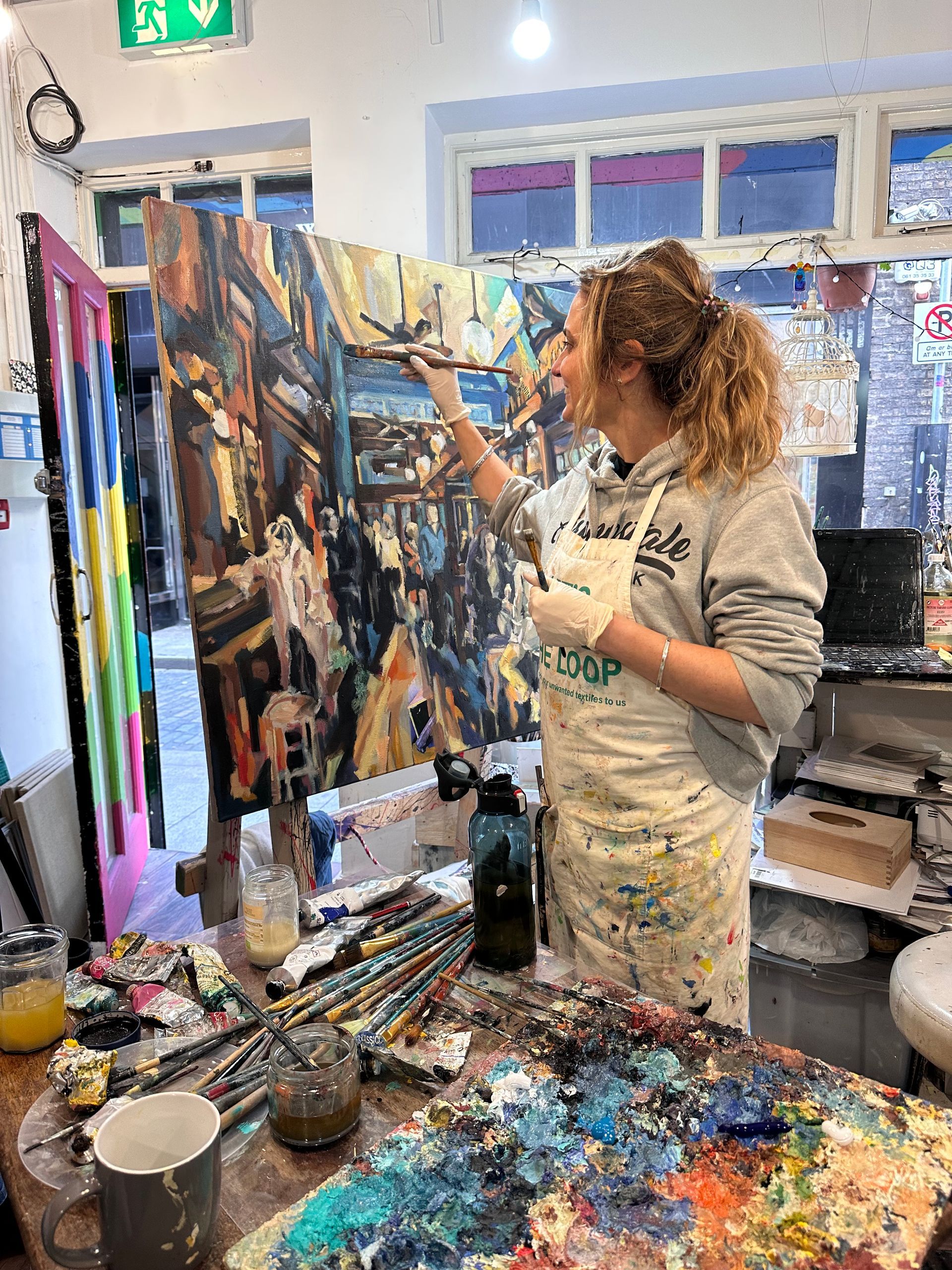 Aga Szot in her art studio. A white female working o a painting in oils with her palette and brushes in the foreground