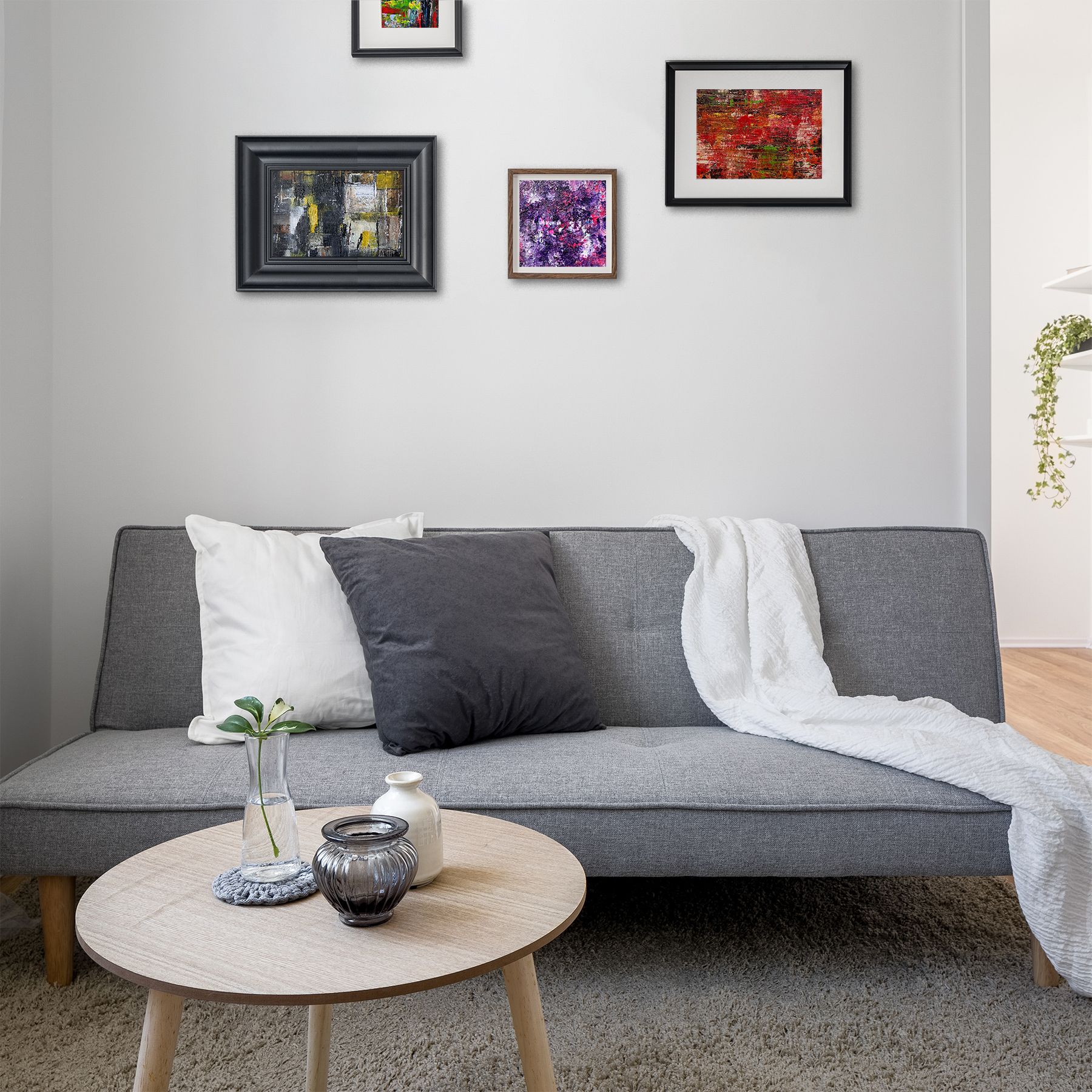 A home gallery wall showing 4 small abstract paintings on a soft grey wall in a room with a grey sofa and coffee table in the foreground