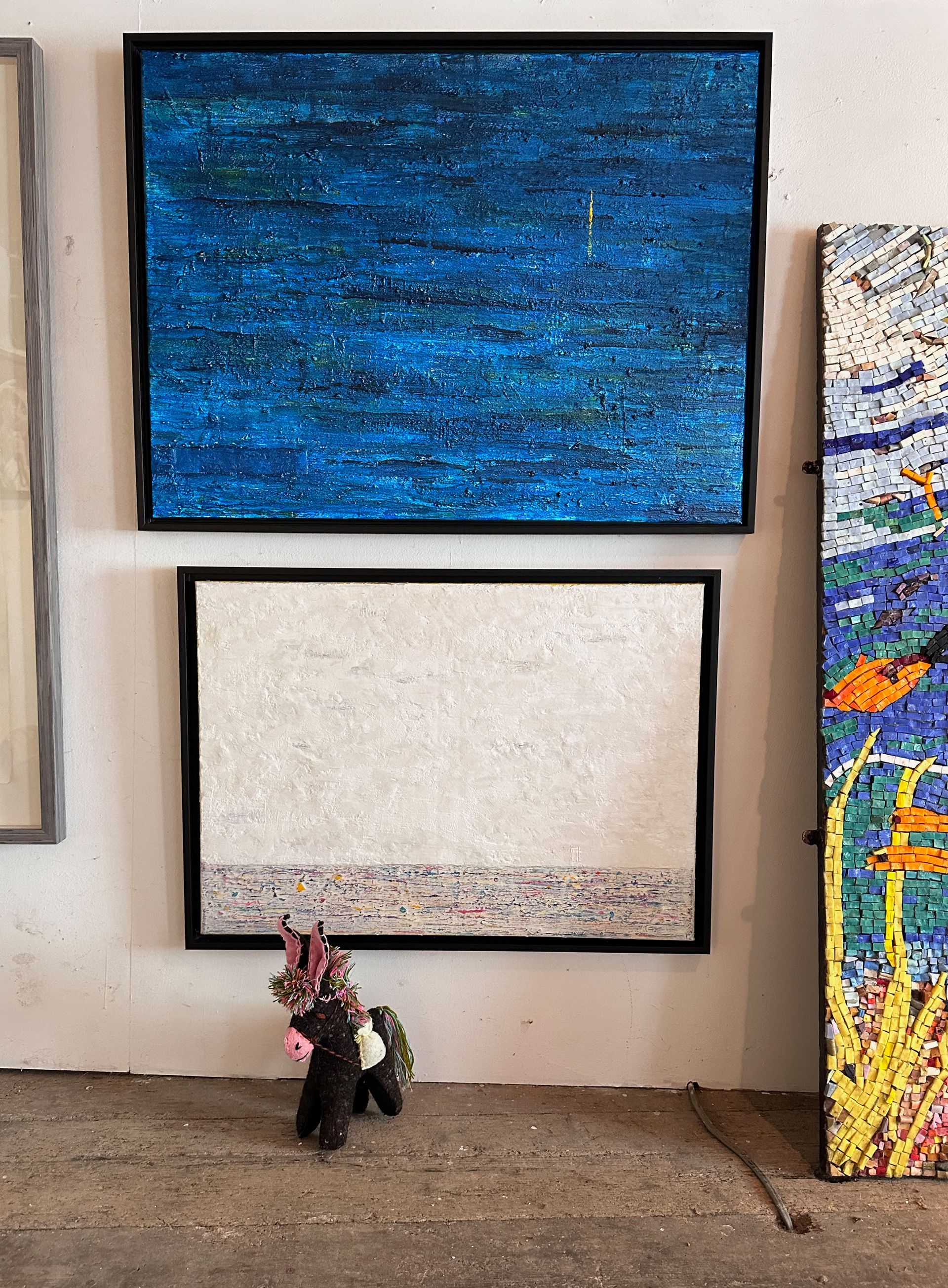 Two abstract paintings hang on a gallery wall at Berkeley Gallery, a small stuffed animal sits on the floor.