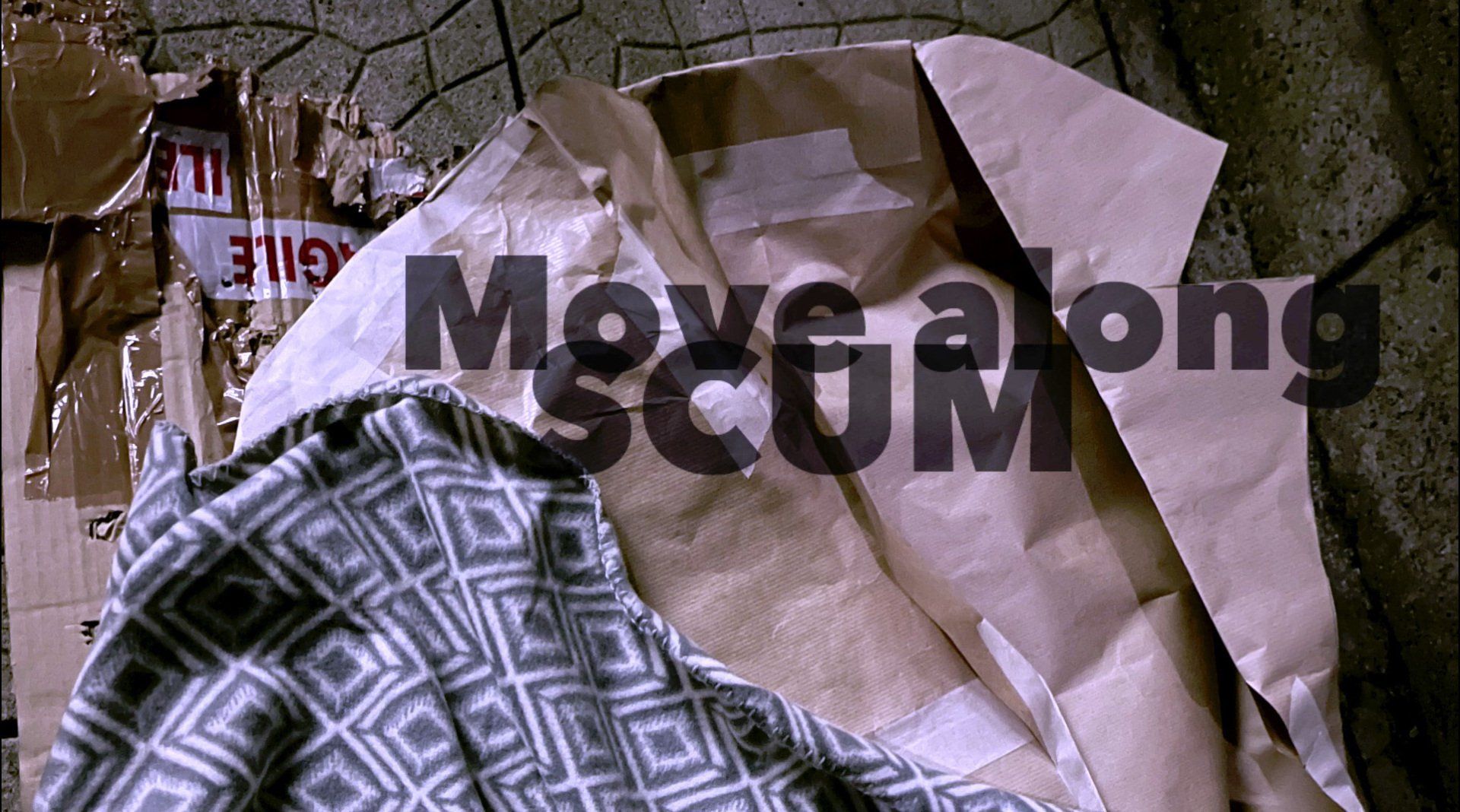 This frame shows a cardboard-covered pavement and a patterned blanket beside a discarded paper coat. The words “Move along SCUM” are starkly overlaid, confronting viewers with the language of exclusion