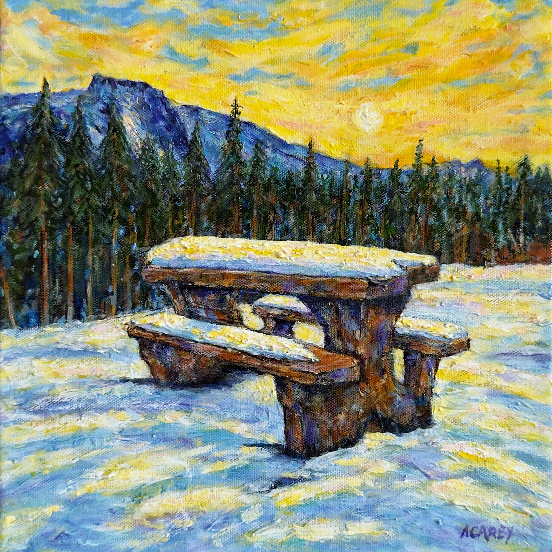 Snow-covered picnic table at sunrise near Welcome to Alberta sign, with pine forest and mountains in the background