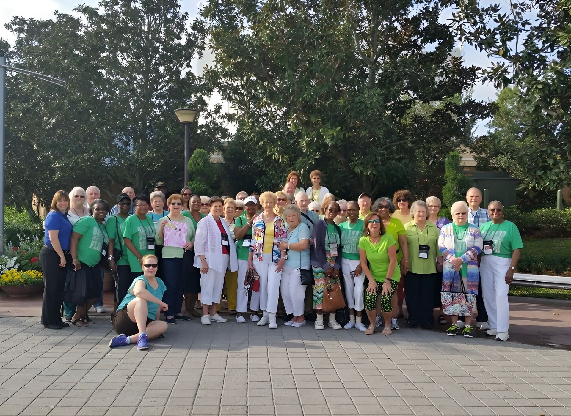 Group of people in green shirts pose outdoors near trees and walkways.