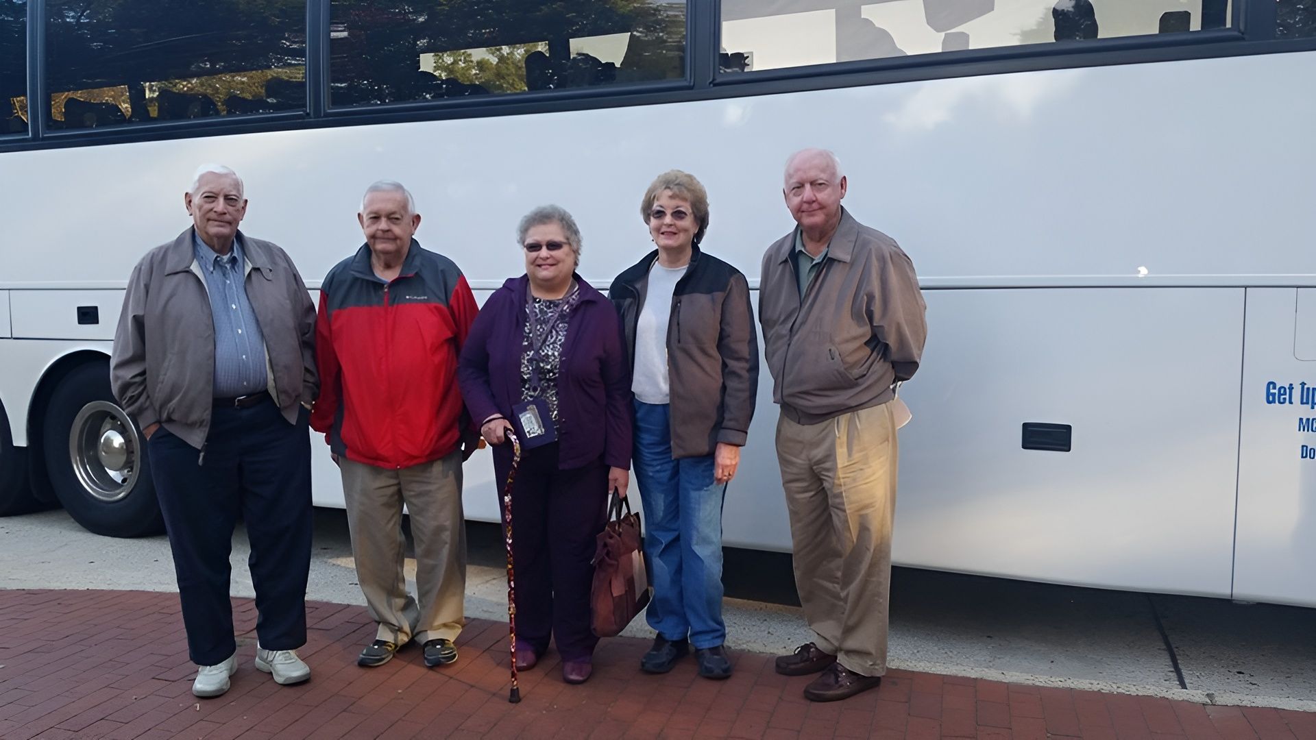 Five people standing in front of a white tour bus. They appear to be in their senior years.