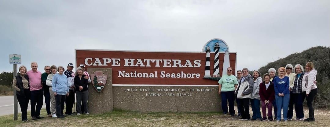 Group poses in front of the Cape Hatteras National Seashore sign on a cloudy day.