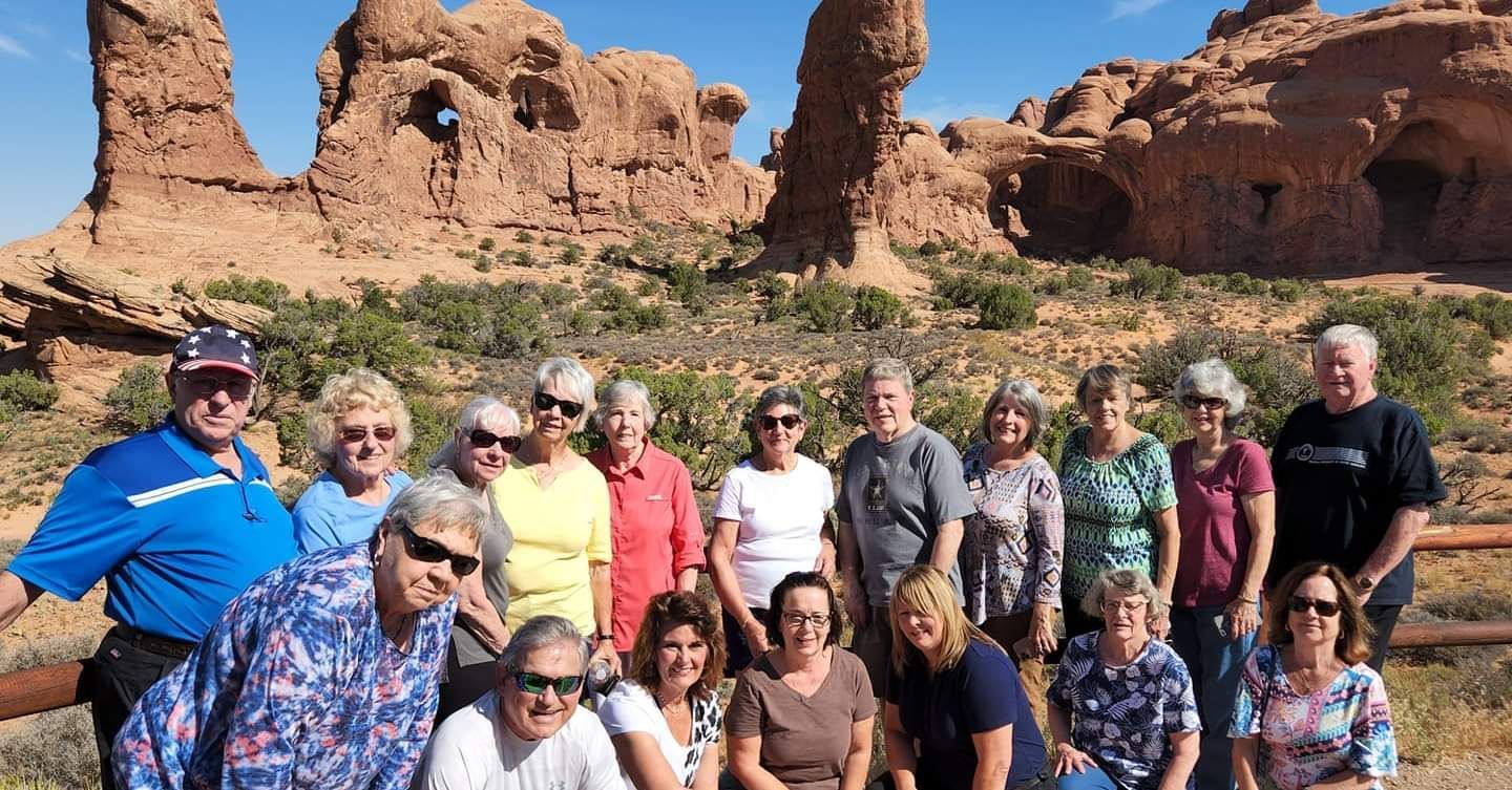 Group of people posing for a photo in front of red rock formations under a blue sky.