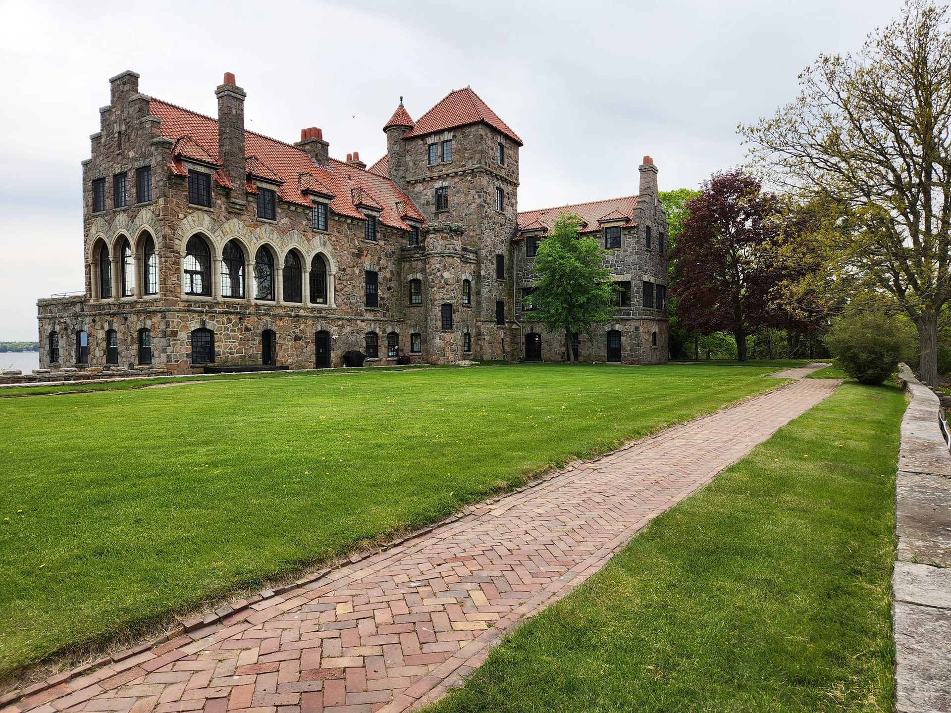 Stone castle with red tile roofs and arched openings, set on a grassy lawn with a brick path.