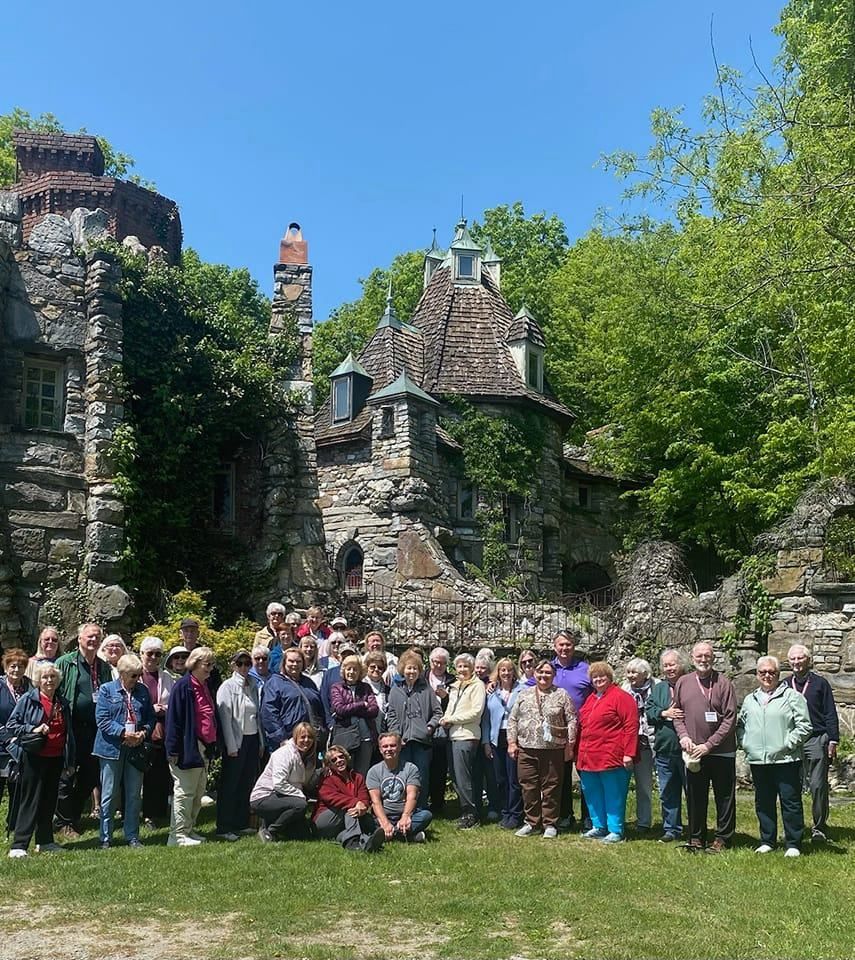 Group of people posing in front of a stone building with turrets and a lush green landscape.