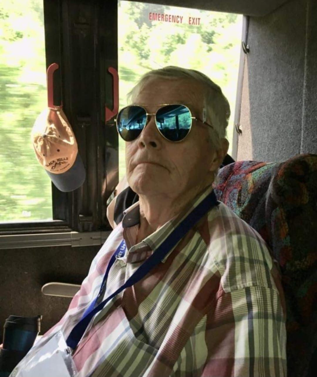 Person wearing sunglasses on a bus, looking upwards. Reflective blue lenses. Plaid shirt.