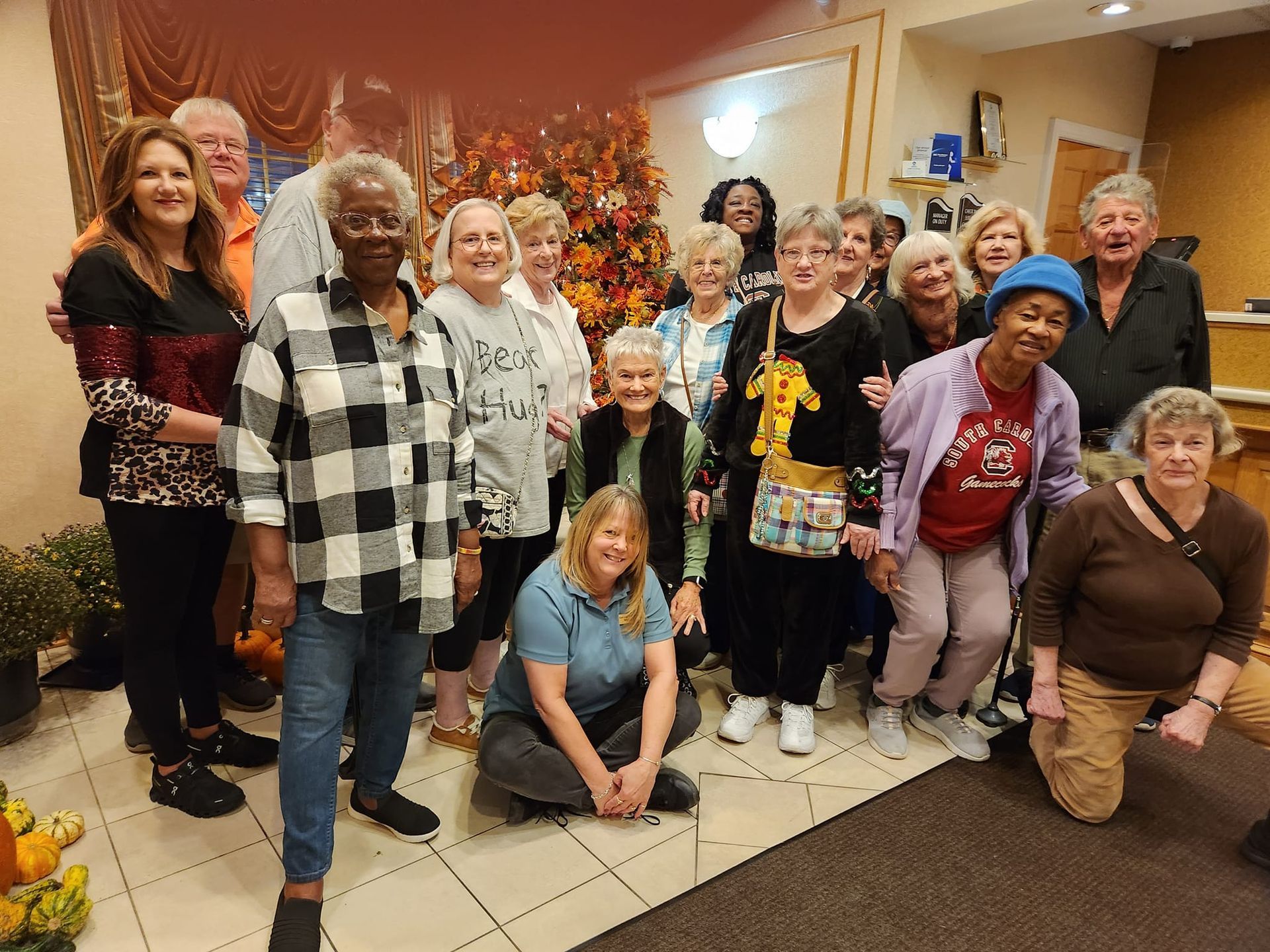 Group of people gathered indoors, near fall decorations. Some are smiling, posing.