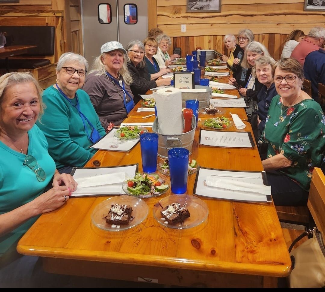 Group of people seated at a long wooden table, eating and smiling in a restaurant.