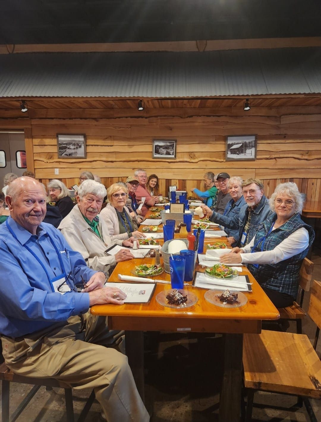 People seated at a long wooden table in a restaurant with log walls, eating food.