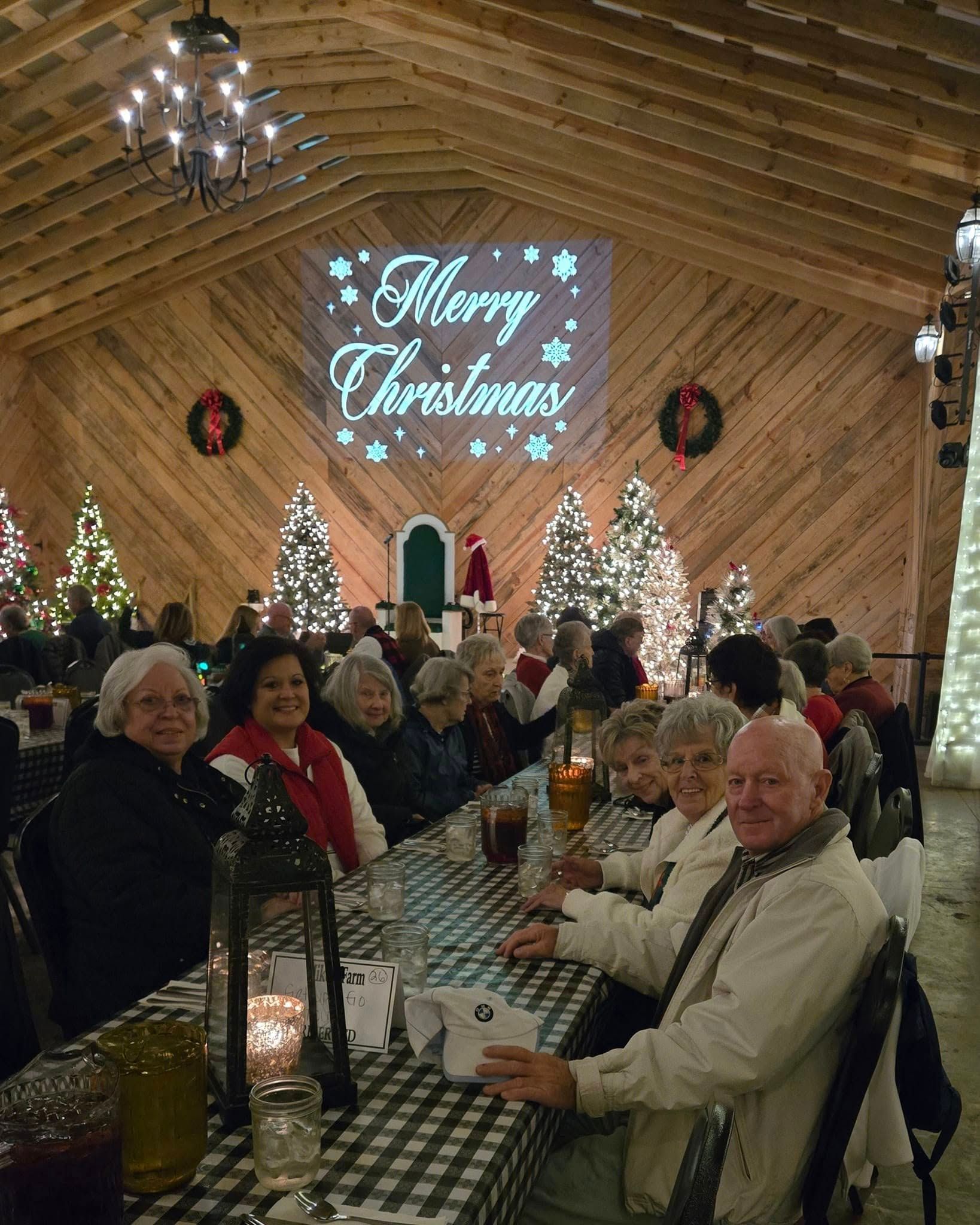 People seated at a table in a decorated hall for Christmas. A “Merry Christmas” display is projected above.