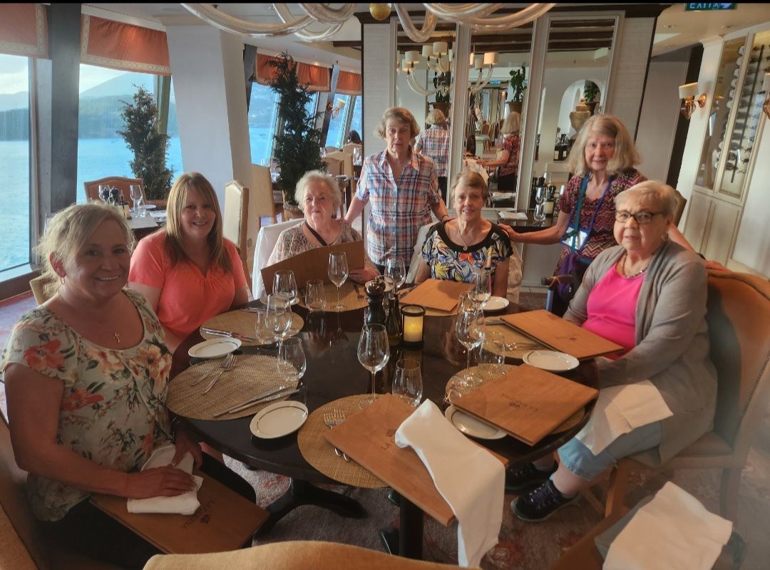 Group of seven people seated around a circular table in a restaurant with a waterfront view.