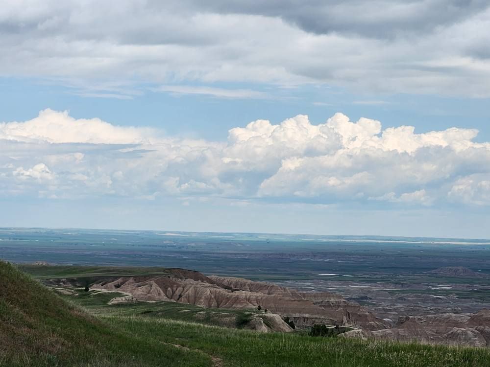 Rolling green hills and reddish-brown rock formations under a cloudy blue sky.