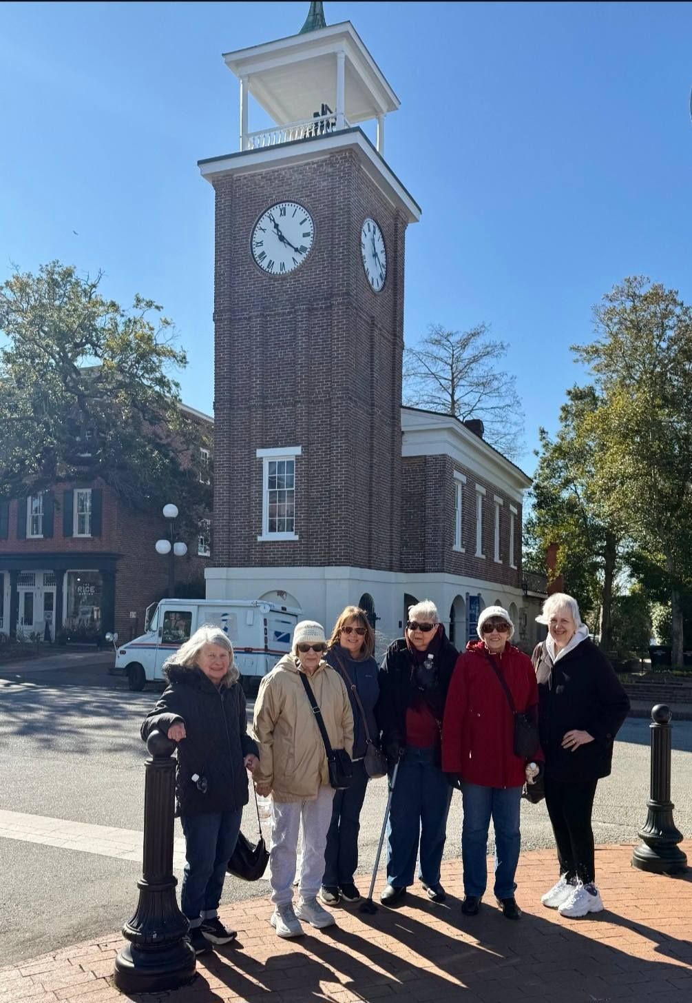 Group of people pose in front of a brick clock tower on a sunny day.