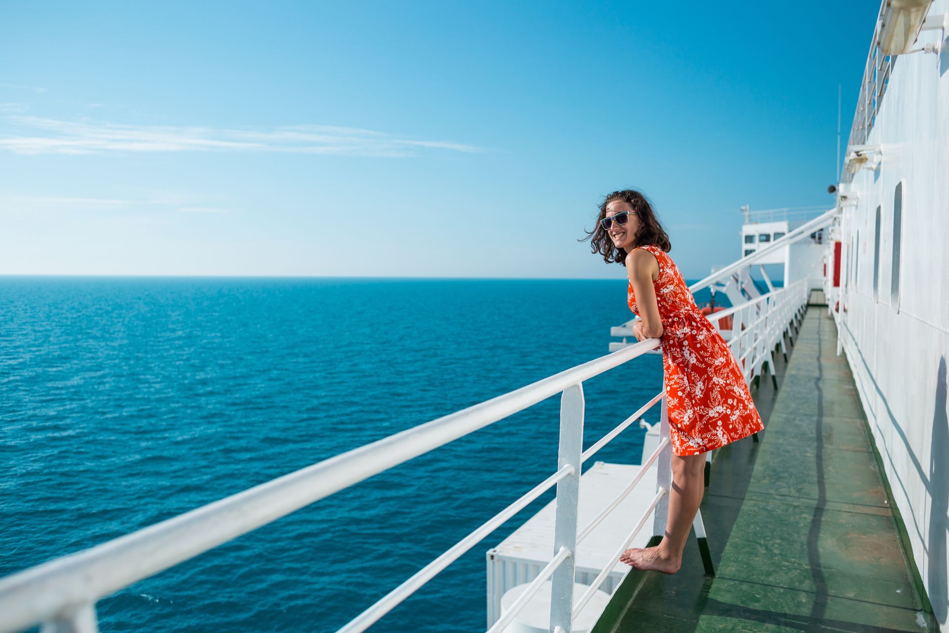 A woman in a red dress is standing on the deck of a cruise ship looking out over the ocean.