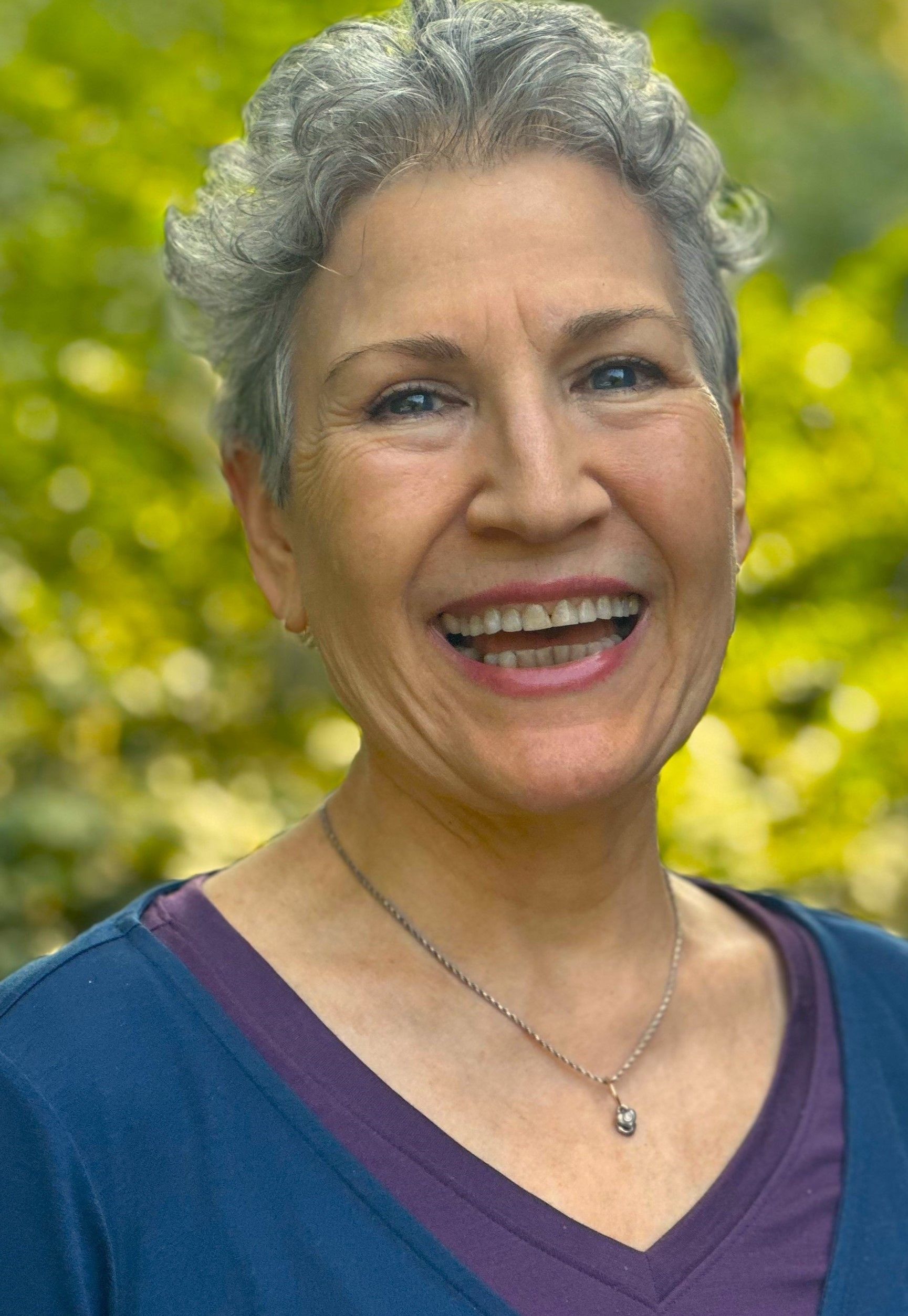 A woman with gray hair and a purple shirt is smiling for the camera.