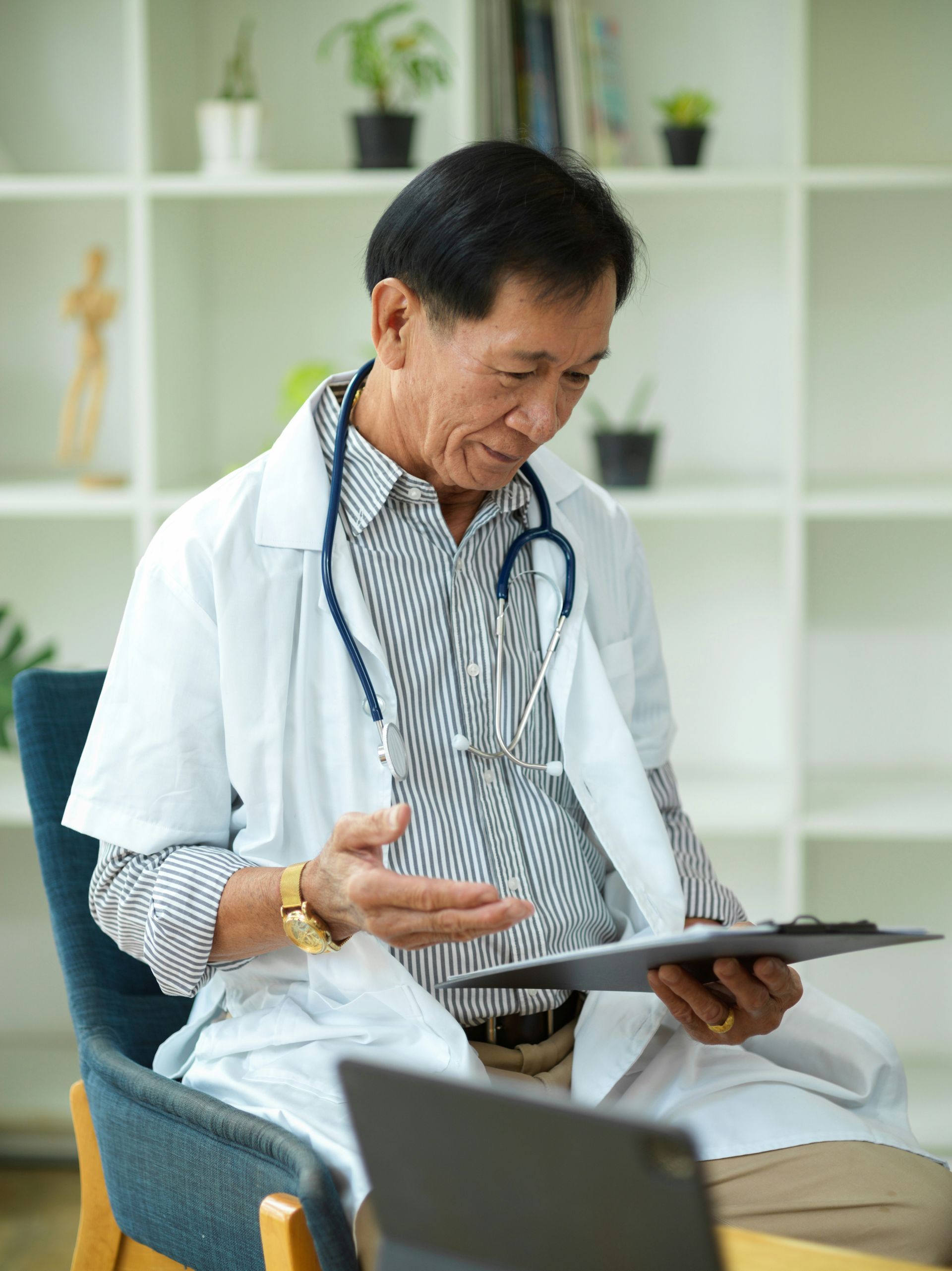 A doctor is sitting in a chair looking at a clipboard.