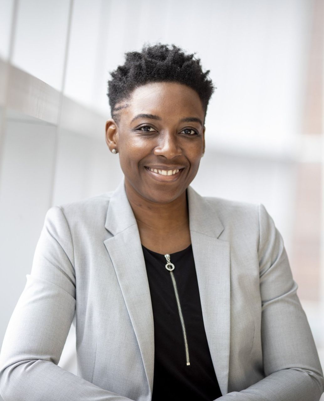 A woman in a grey jacket and black shirt is smiling for the camera.