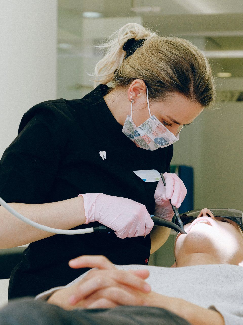 A woman wearing a mask and pink gloves is working on a patient 's teeth