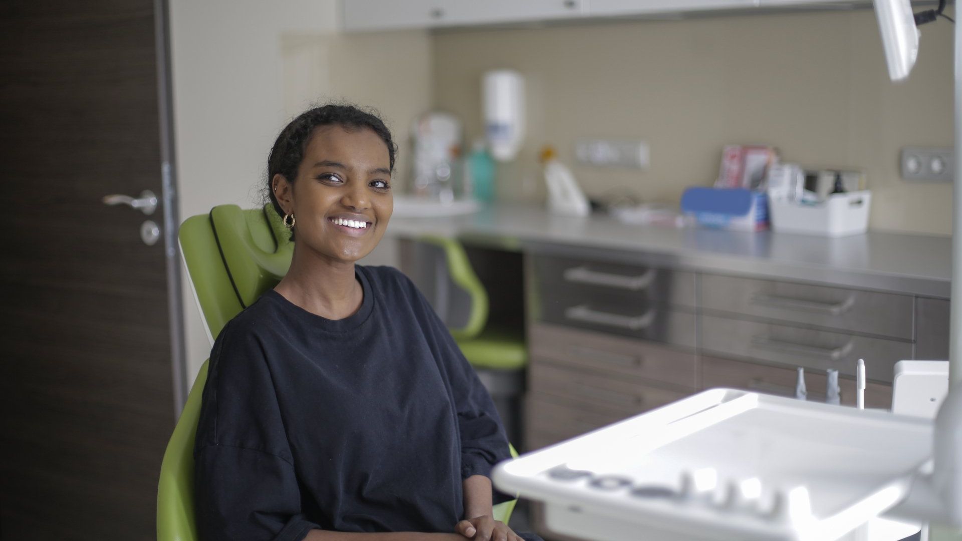 A woman is sitting in a dental chair and smiling at the camera.