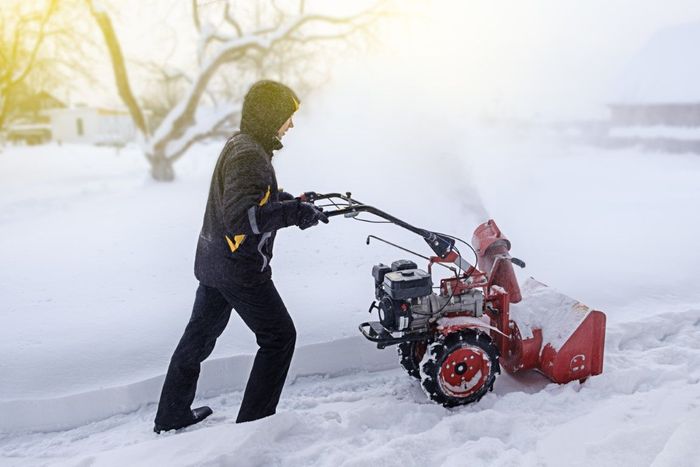 Person using a red snowblower to clear a snow-covered path.