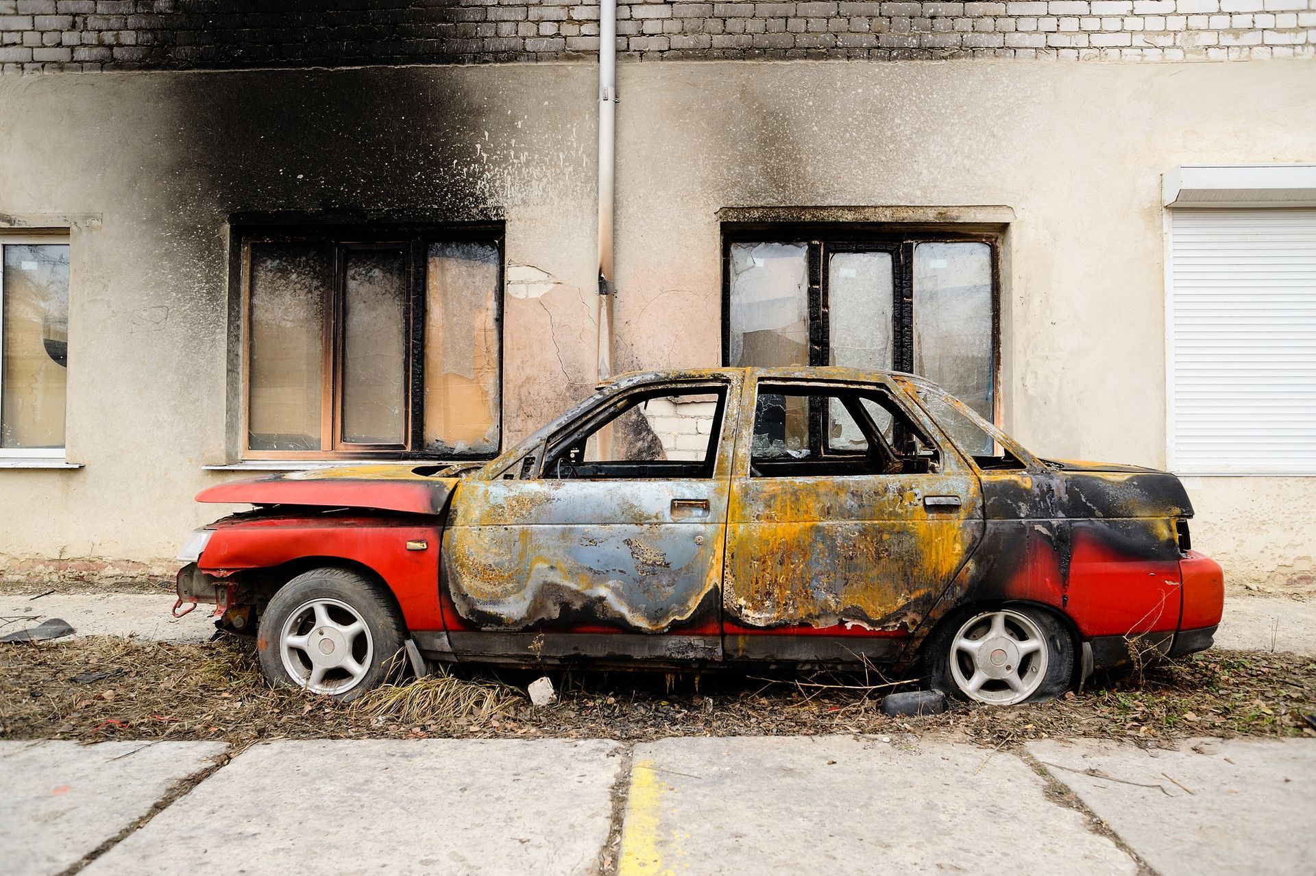 A burned car parked in front of a property.