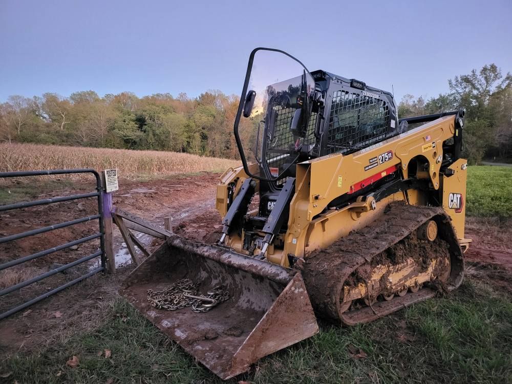 Yellow Caterpillar track skid steer loader near a gate and field.