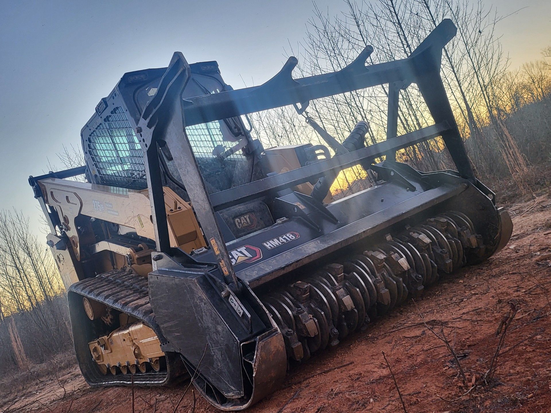 A track skid steer with a forestry mulcher attachment in a wooded area.