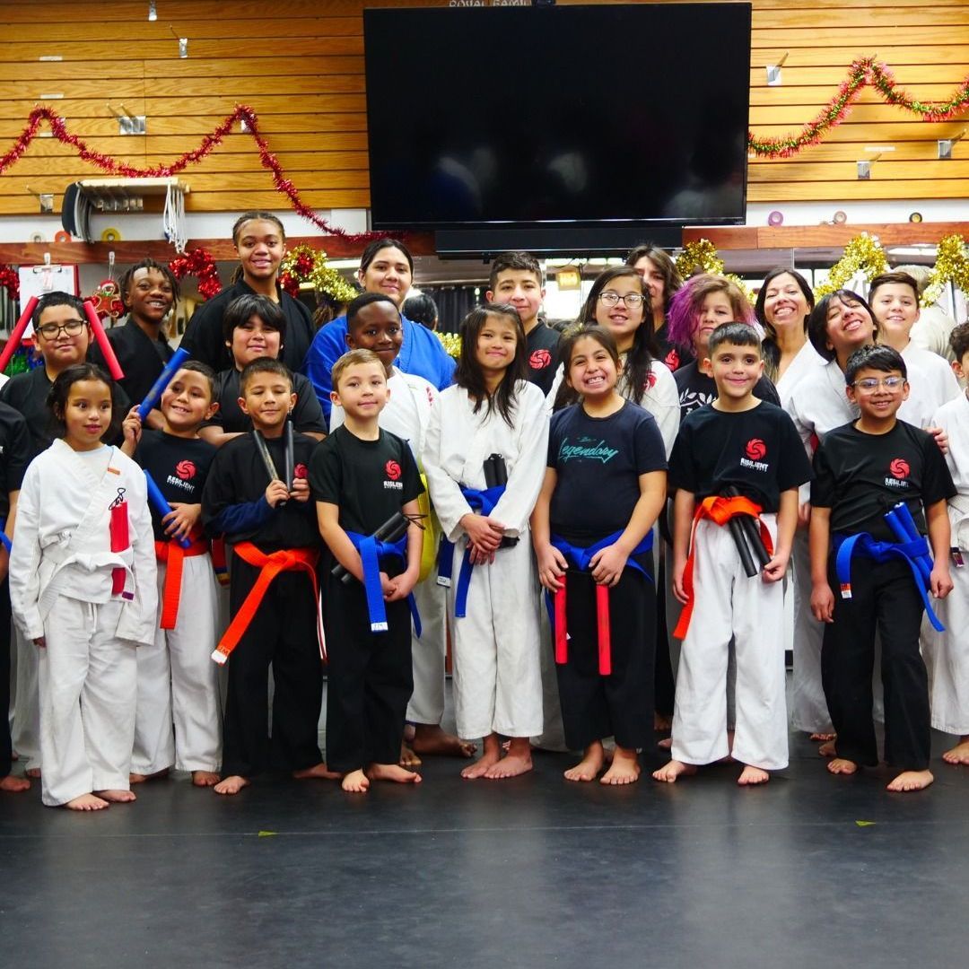 A man is kneeling down next to a young boy in a taekwondo class.