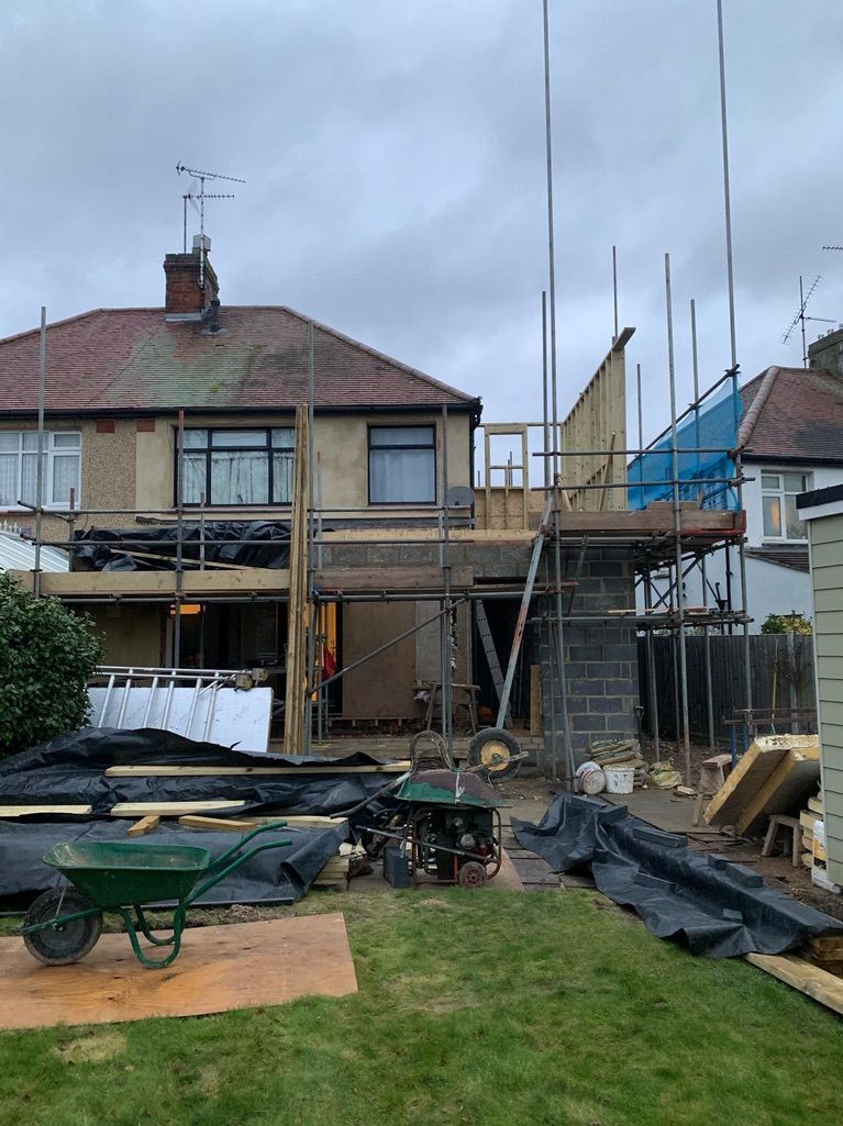 a house is being built with scaffolding and a wheelbarrow in front of it .