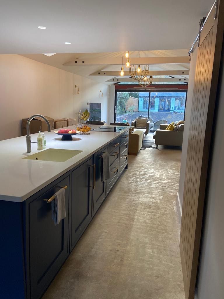 a modern kitchen with blue cabinets and white counter tops leading to a living room .