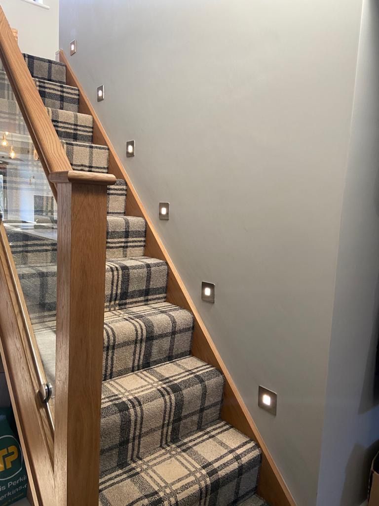 a wooden staircase with a plaid carpet and a glass railing .
