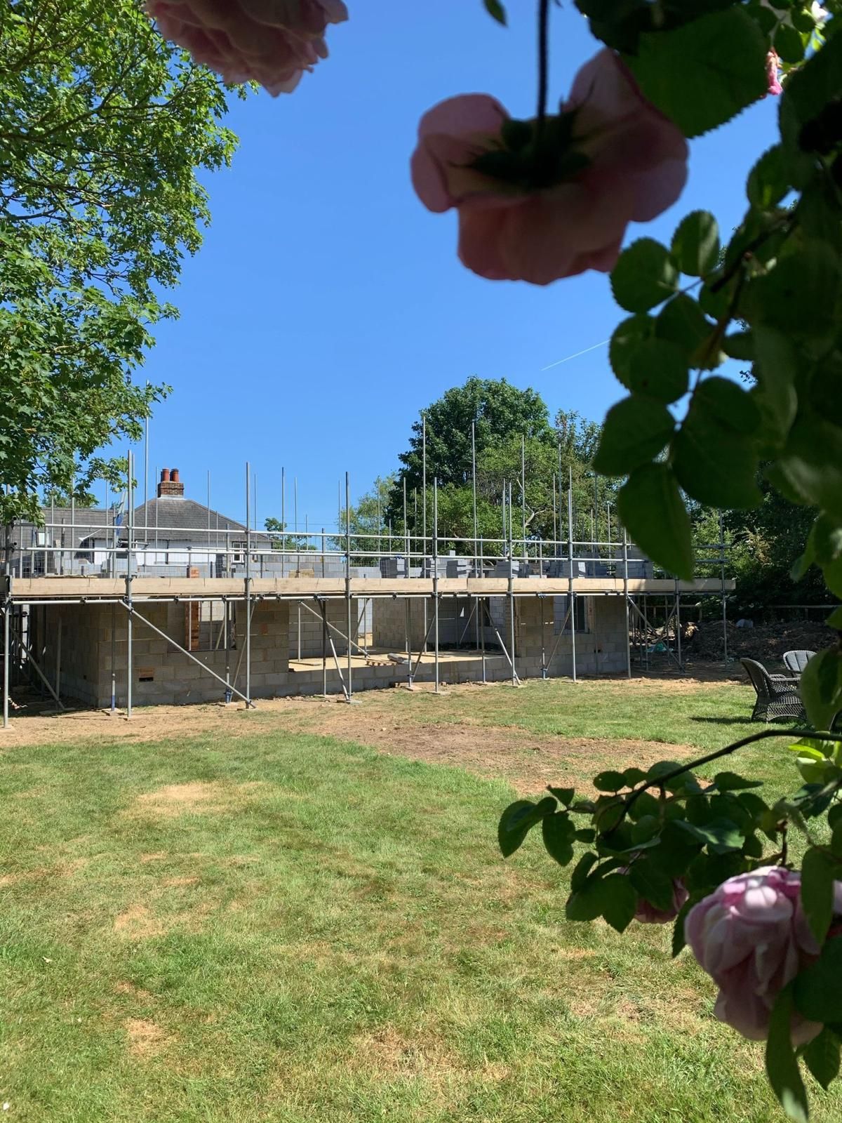a house is being built in a field with scaffolding and flowers in the foreground .