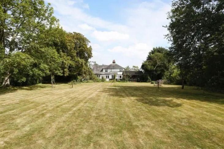 new build site on a large lawn with a house in the background and trees in the foreground .