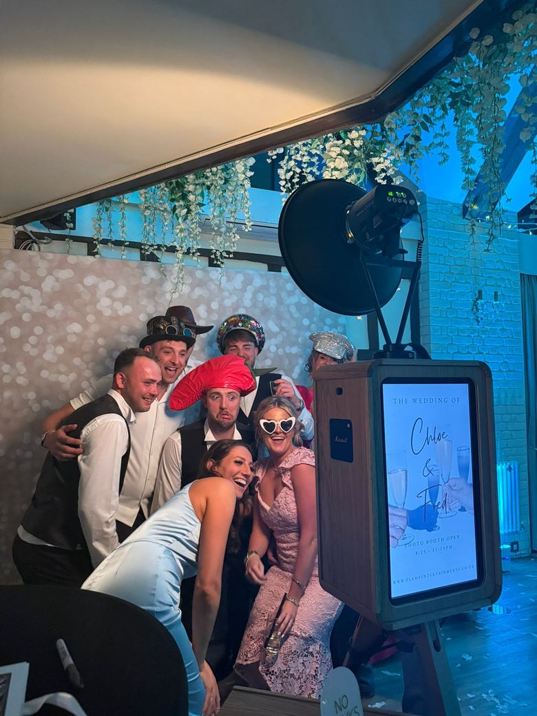 A group of people wearing party hats and glasses pose for a photo in front of a photobooth.