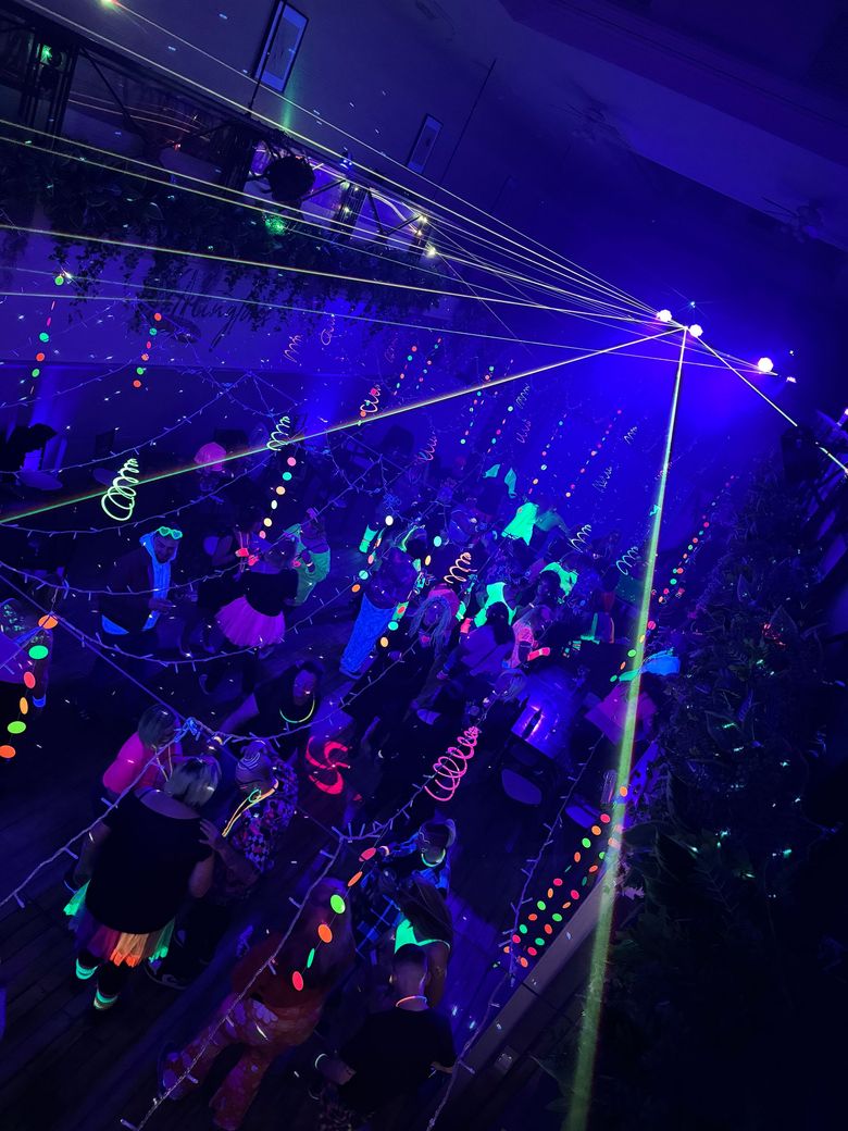 A high-angle view of a crowd dancing in a dark room illuminated by vibrant blue laser beams and string lights.