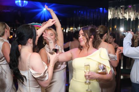 People dancing at a party, including someone in a yellow dress holding a drink.
