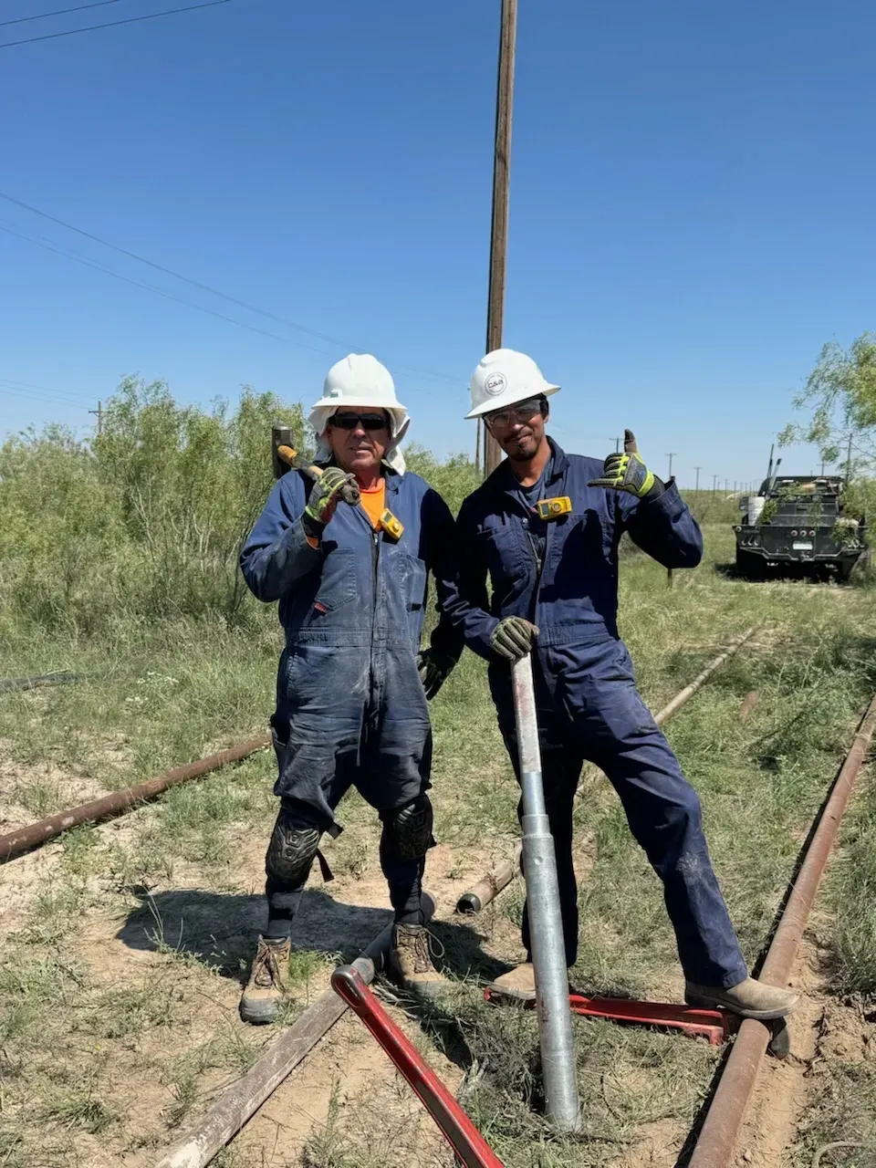 Two men in hard hats are standing next to each other in a field.