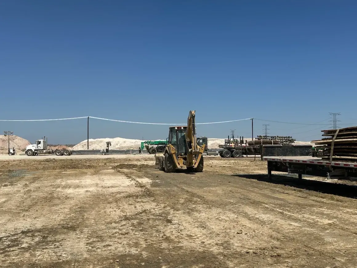 A bulldozer is driving through a dirt field next to a truck.
