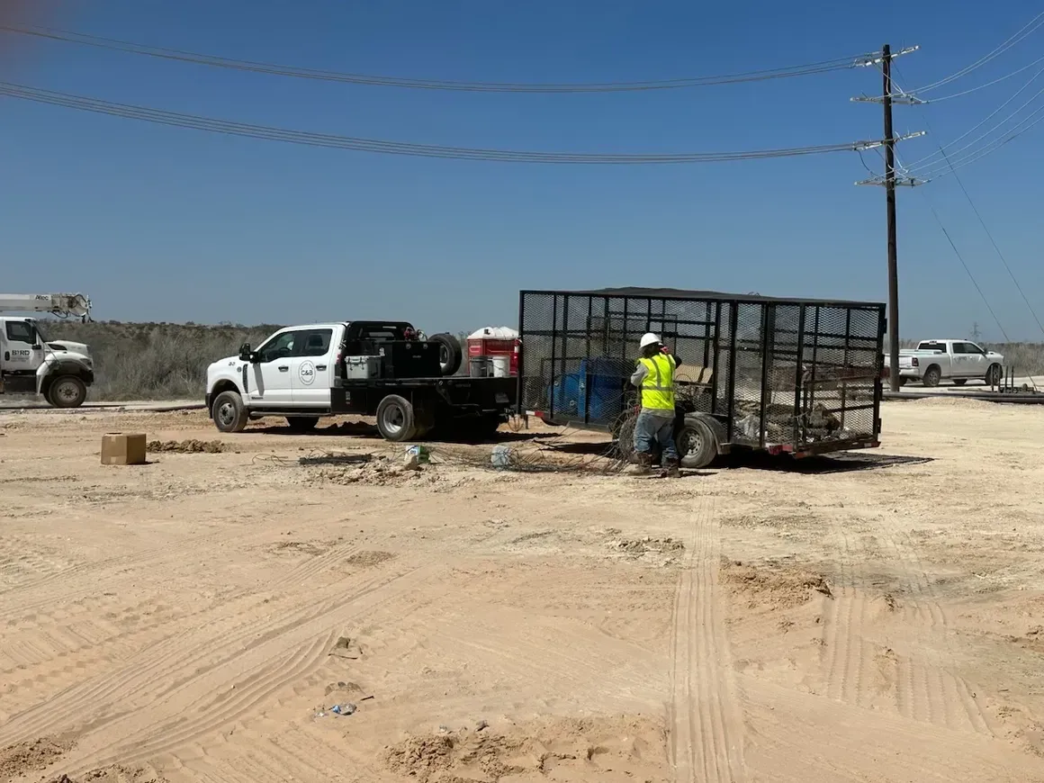 A man in a yellow vest is standing next to a truck in a dirt field.