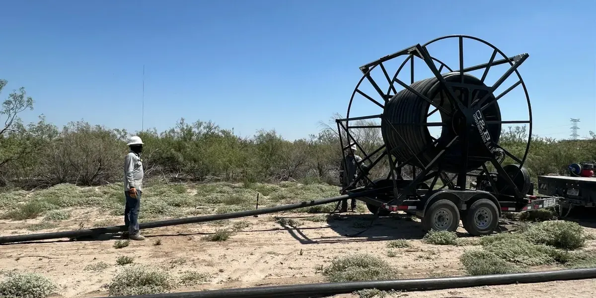 A man is standing next to a large hose reel in a field.