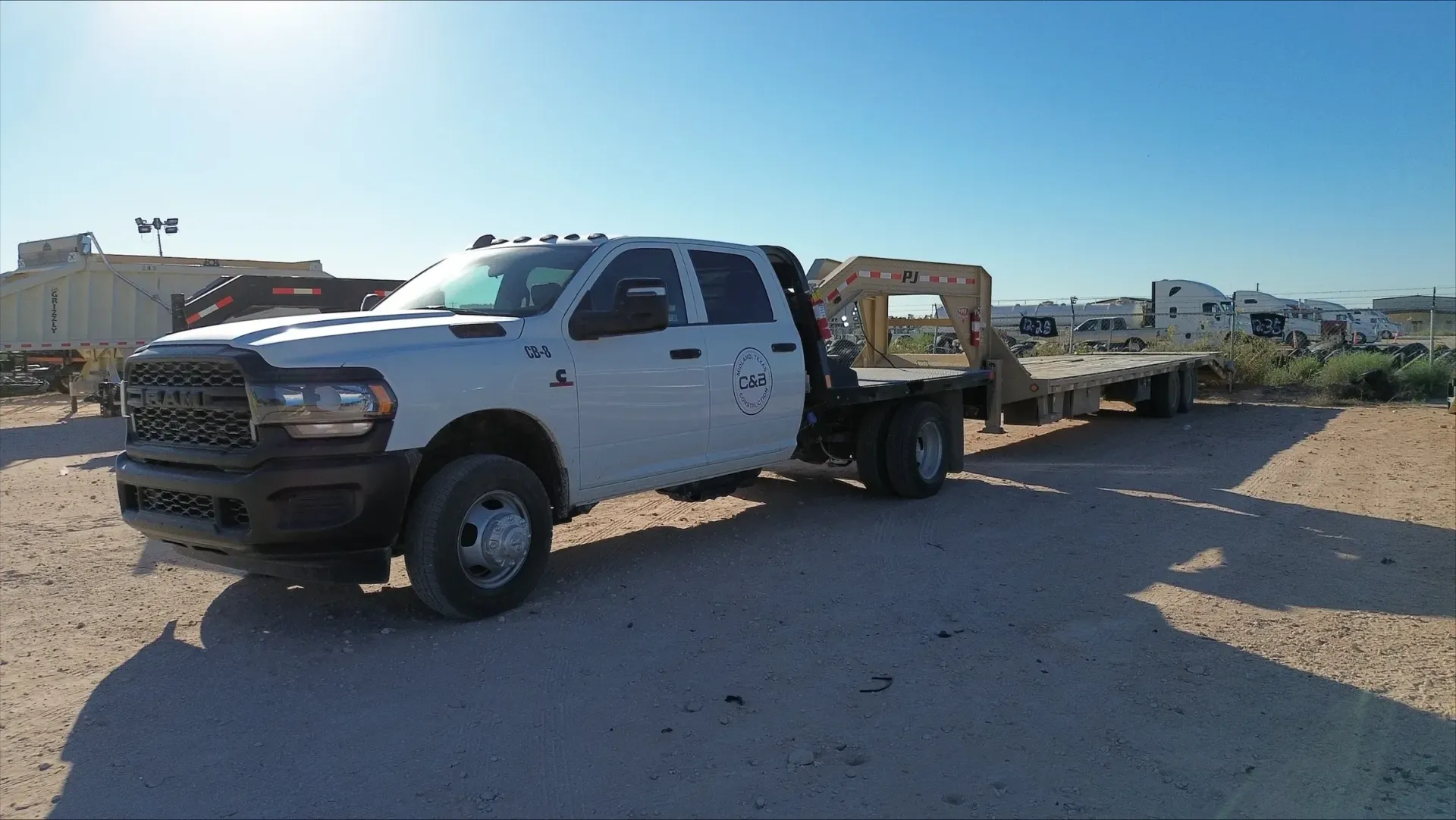 A white truck with a flatbed trailer attached to it is parked on a dirt road.