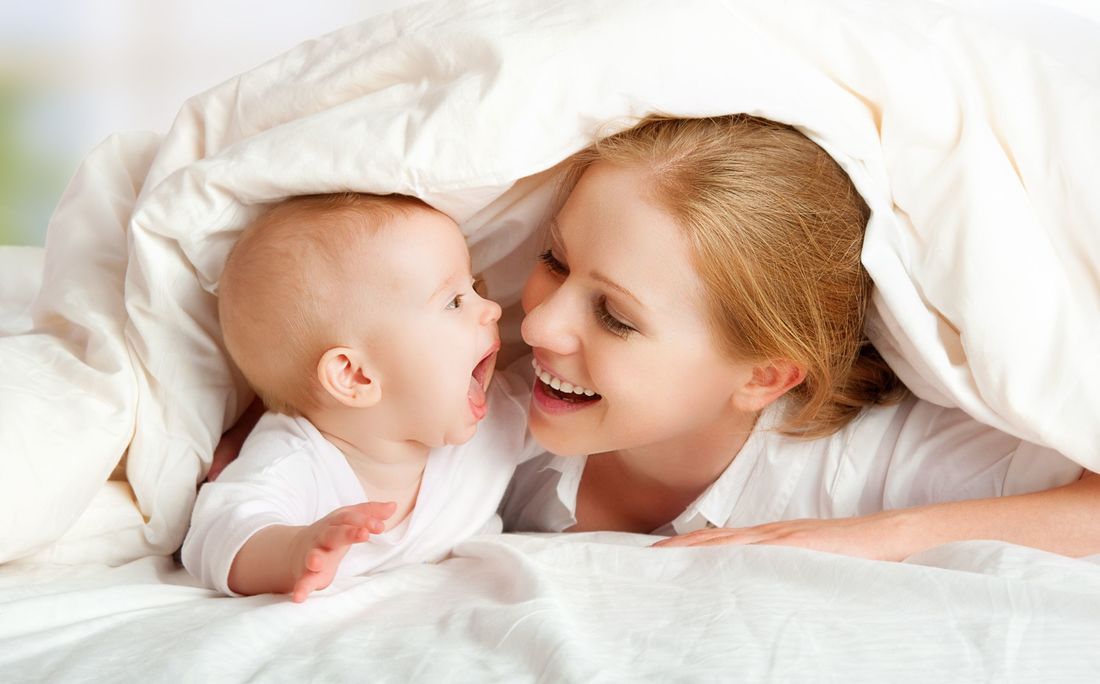 Woman and baby smiling under a white blanket, close-up.