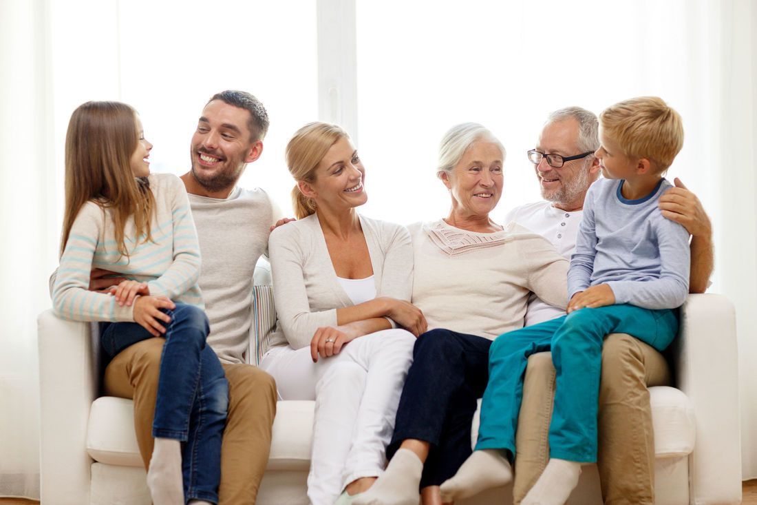 Family of seven sitting on a white sofa smiling.