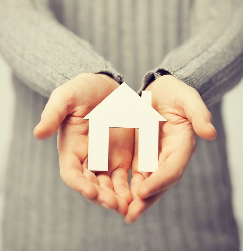 Hands holding a small, white paper house, symbolizing homeownership.