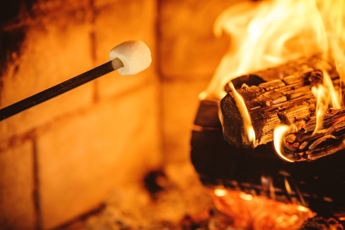 Marshmallow on a stick being roasted over a crackling fireplace with glowing flames.